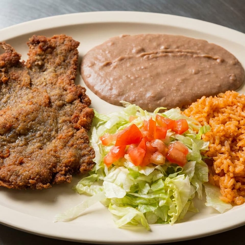 Plate of breaded fried steak with refried beans, Mexican rice, and lettuce salad topped with diced tomatoes.