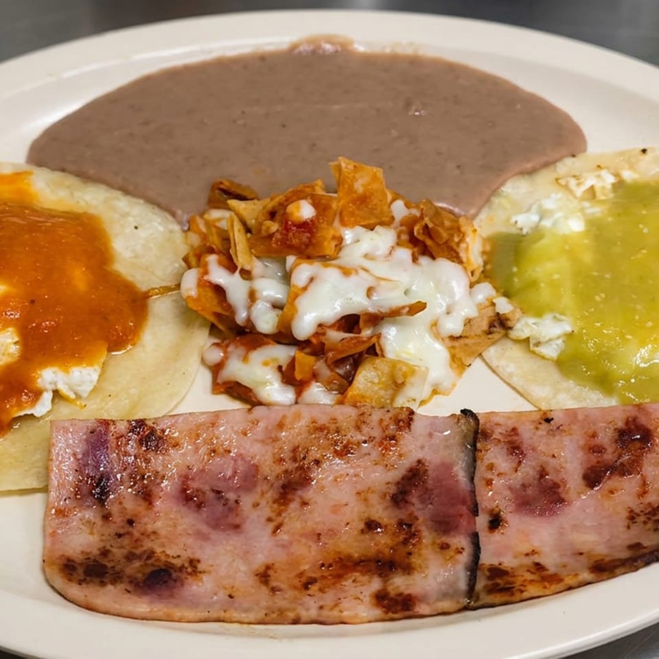 Mexican breakfast plate with eggs in red and green salsa, refried beans, cheesy chilaquiles, and grilled ham.