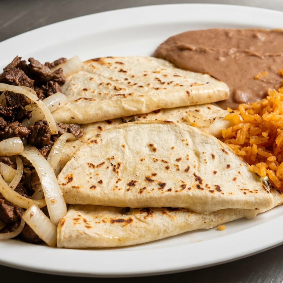 Plate of grilled steak with onions, folded flour tortillas, Mexican rice, and refried beans.